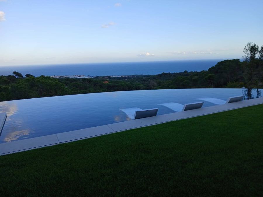 Piscina desbordante y jardín de una vivienda unifamiliar construida por DM2, con el mar al fondo
