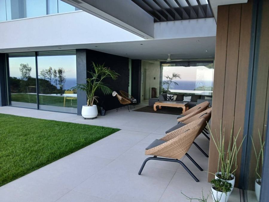 Porche cubierto y jardín de una vivienda unifamiliar, con el mar al fondo